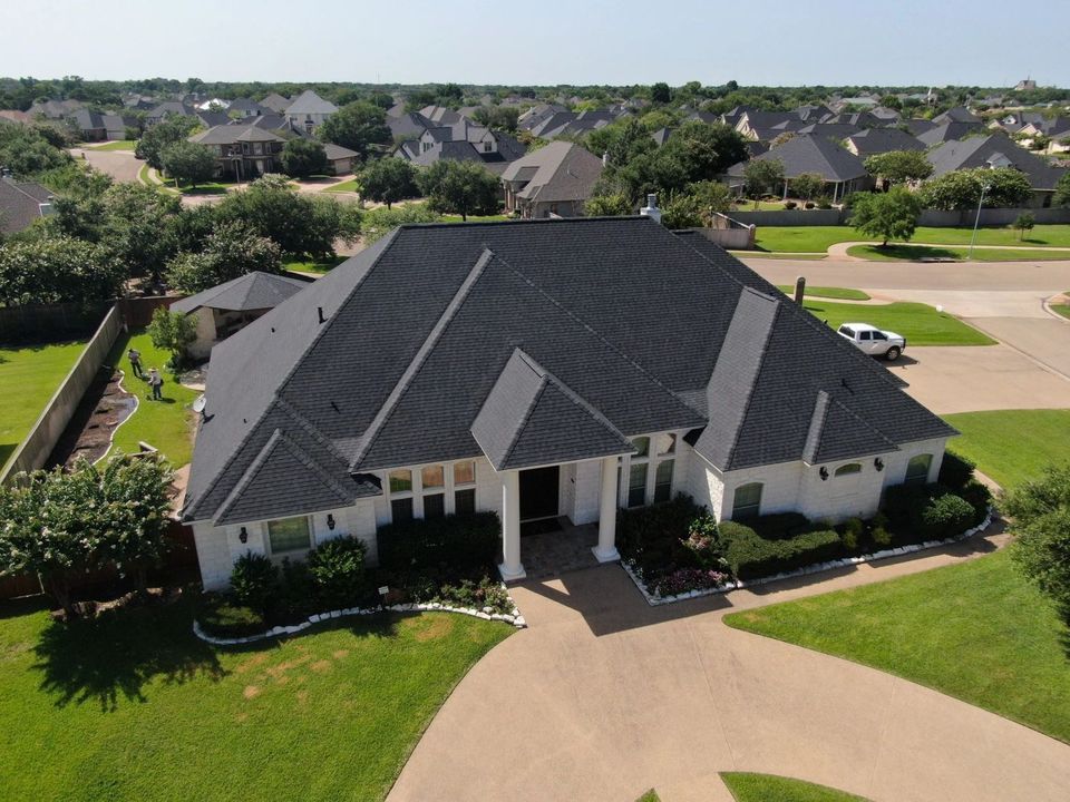 White stone home with a dark architectural shingle roof in a Texas neighborhood